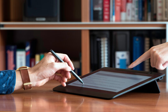 Close-up of two hands interacting with a digital signature pad. One person holds a stylus to sign, while the other points at the screen. Business and technology concept.