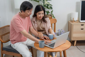 Older couple collaborating on laptop while enjoying coffee at home.