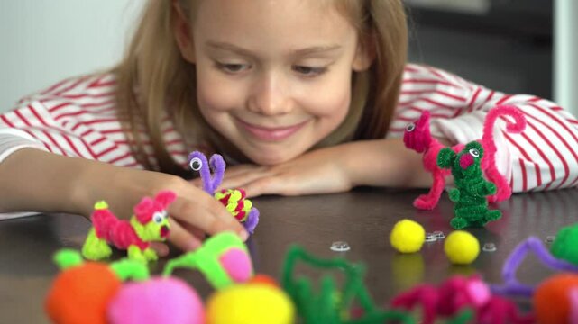 Close up of little girl fun make diy from colored chenille wire and plays with toy. Creation handmade craft. Children leisure