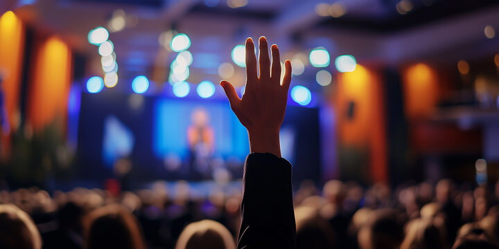 Enthusiastic audience member raises hand during an engaging presentation at a professional conference in a well-lit auditorium setting