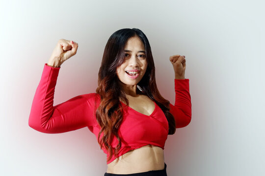 Asian woman wearing casual t-shirt standing over isolated white background showing arms muscles smiling proud. Fitness concept.