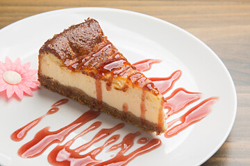 Creamy new york cheesecake slice served on white plate with decorative strawberry coulis and pink sugar flower