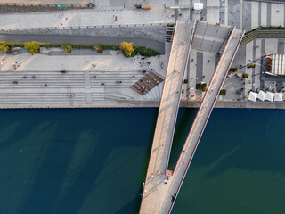 pedestrian bridge over blue Vistula river, people walking at shore and embankment, Warsaw, aerial top view