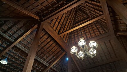 Obraz premium Traditional Javanese Roof with Wooden Pillars and Hanging Lantern – High-Quality Photo for Architectural Backgrounds, Ethnic Interiors, and Cultural Heritage Concepts
