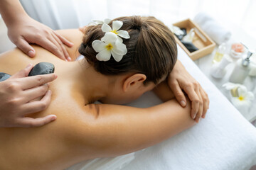 Hot stone massage at spa salon in luxury resort with day light serenity ambient, blissful woman customer enjoying spa basalt stone massage glide over body with soothing warmth. Quiescent