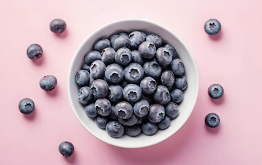 A white bowl filled with ripe blueberries on a pink background