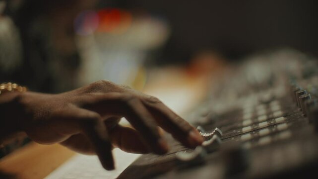 Hand of Black sound engineer adjusting faders on professional audio mixer in recording studio. Close-up view