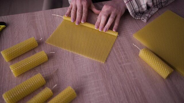 DIY and hobbies concept. Female hands making beeswax aroma candles from wax sheet in home workshop.