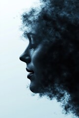 A woman with voluminous curly hair is captured in profile against a softly lit background. The lighting enhances the contours of her face, giving it a dreamy and artistic feel