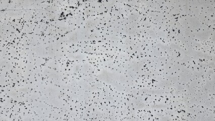 Old grey concrete wall texture with cracks and stains. The building walls have black stains and several black holes.