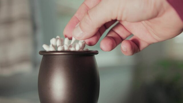 Slow-motion closeup of a black container of cotton ear buds, and a hand picking one of them