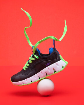 Black sports sneakers reebok with bright green sole and ball on red background.