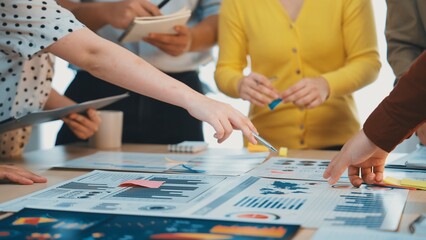 A diverse group of professionals engages in a collaborative meeting, analyzing business charts and graphs, discussing strategies and planning projects in a modern office setting. SACTR