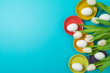 Easter holiday creative concept  with easter eggs, colorful plates and white tulips flowers on blue background. Top view, flat lay