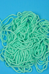 A close-up view of a tangled pile of light green yarn against a solid blue background, showcasing its texture and disarray
