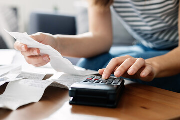 Close-up view young homeowner woman hands sitting on sofa using calculator an laptop to calculate...