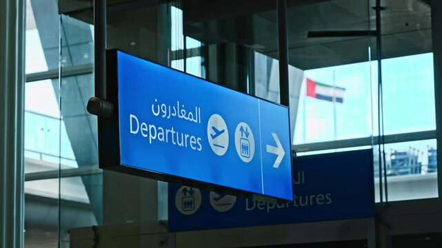 A blue departures information board with arrow and flight signs. Direction sign in Arabic. Dubai airport UAE flag on background