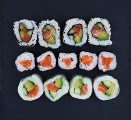Assortment of sushi on a slate in top view. Japanese delicacy with a diameter of a few centimeters with cooled cooked rice, salmon, avocado, cucumber,...