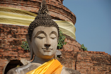 sacred Buddha stone statue in Ayutthaya, Thailand, draped with orange silk scarves, symbolizing...