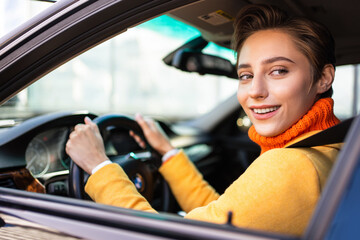 Fototapeta premium Beautiful young woman with short hair drives car in the city