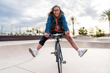 Beautiful senior woman cycling with urban bicycle at city park - Mature adult female cyclist having...