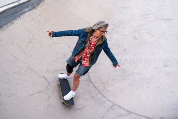 Beautiful active senior woman skateboarding at skate city park - Mature adult female skateboarder having fun, concepts about elderly, modern lifestyle and green mobility