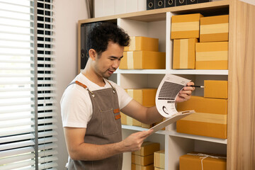 A man is standing in front of a shelf full of boxes and looking at a tablet. He is holding a box in his hand

