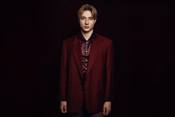 Handsome Male Model Stands in Black Room Wearing Red Jacket, Looking at Camera with No Emotion and...