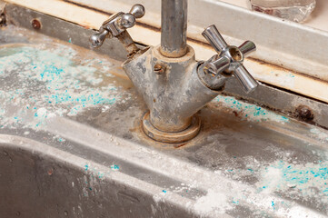 Close-up of a corroded faucet and stained sink showcasing mineral deposits and a lack of cleaning and maintenance.