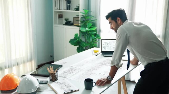 Architect engineer using laptop planning house design at office while sitting at meeting table with blueprint and equipment scatter around.Skilled civil engineer working at blueprint. Alimentation.