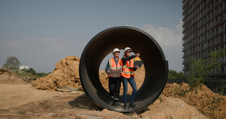 The project engineer team with orange safety vests  holds laptops and blueprint drawings working at...