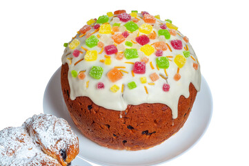 A delicious Easter cake with icing and candied fruit sits on a white plate next to pastry.