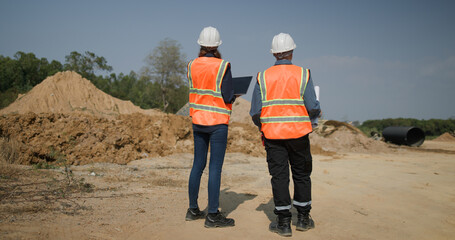 The project engineer team with orange safety vests  holds laptops and blueprint drawings working at...
