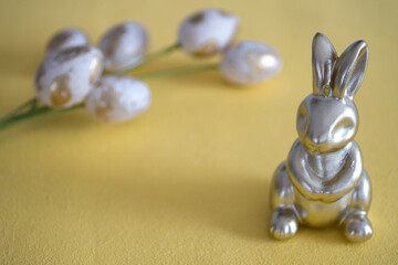 A golden Easter bunny figurine placed on a vibrant yellow background, accompanied by white and gold decorative eggs. 