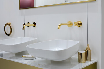 bathroom has two sinks, one of which is a gold-colored bowl. sink is surrounded by a white countertop and has a gold soap dispenser. bathroom also has a mirror above the sinks