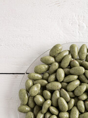 Chocolate-covered nuts on a white wooden background. Green candies on a glass plate.