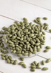 Almonds in chocolate glaze. Green candies on a white wooden background.