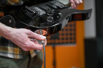 Person plugging in electric guitar cable in recording studio