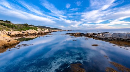 Fototapeta premium Serene coastal view of calm water reflecting clouds and rocky shoreline under a vibrant blue sky : Generative AI