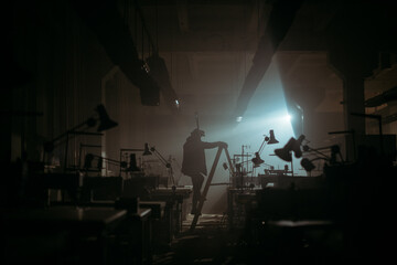 A mysterious silhouette of a man in the light of a lantern in the scary, foggy space of an abandoned factory, sewing workshop