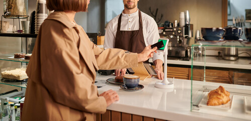 An electronic payment terminal on the counter of a coffee shop. The girl pays for the purchase with a mobile phone through the app, the barista is behind the counter