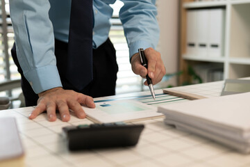 A man is pointing at a piece of paper on a desk. The paper has a business-related title and the man...