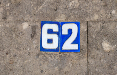 Street address number, number 62. Blue tiles with white numbers inset into a concrete wall.