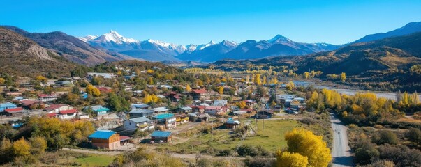 Obraz premium Aerial view of scenic mountain village in autumn with snow-capped peaks and vibrant foliage