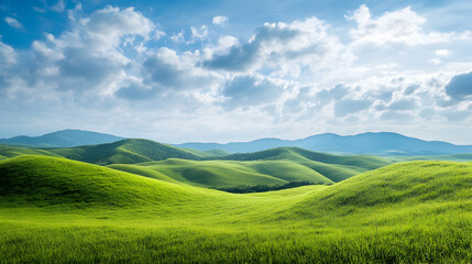 Fototapeta premium Rolling green hills under a cloud-dotted sky with lush grass and distant mountain silhouettes in daylight