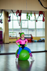 Naklejka premium A small, beautiful girl, in athletic form, trains in the gym with a fitball