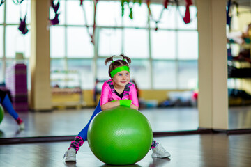 Naklejka premium A small, beautiful girl, in athletic form, trains in the gym with a fitball