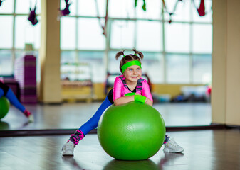 Naklejka premium A small, beautiful girl, in athletic form, trains in the gym with a fitball