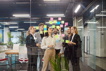 Young business people men and women posting notes and reminders in office preparing for meeting or...