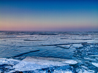 Gefrorener See mit Eisschollen bei Sonnenaufgang
Malerische Winterlandschaft mit treibenden Eisschollen auf einem gefrorenen See. Der Himmel leuchtet in sanften Farben.